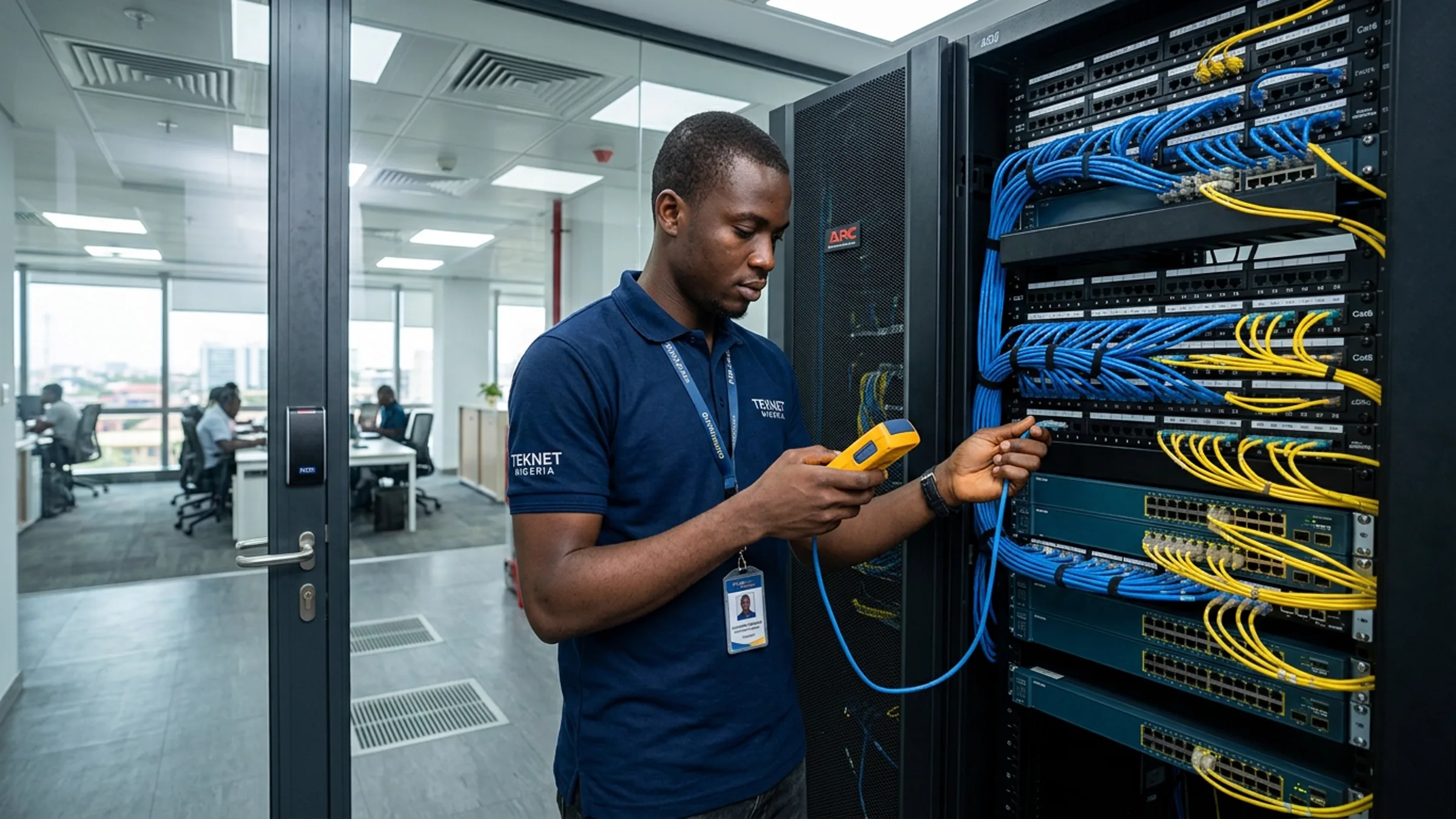 Nigerian engineer testing structured cabling at a server rack in a corporate communications room with open-plan office visible behind glass
